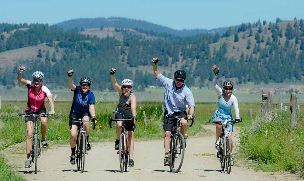photo of friends riding the Tour de Manure, arms raised in the air with pine-covered mountain peaks in the background